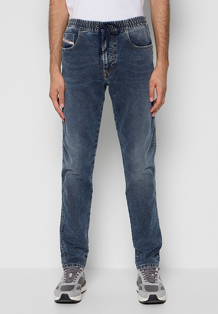 Mann trägt blaue Denim-Jogger-Jeans mit elastischem Bund und Kordelzug, kombiniert mit grau-weißen Sneakers.