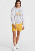 Hellgrauer Hoodie mit grafischem Druck, kombiniert mit gelben Shorts. Das Outfit hat eine lockere Passform und wird mit weißen Sneakers getragen.