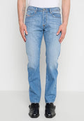 Mann trägt hellblaue Jeans mit geradem Bein, weißes Hemd und schwarze Lederschuhe, steht vor einem einfarbigen Hintergrund.