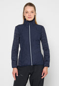 Frau trägt eine marineblaue gesteppte Jacke mit gemusterten Ärmeln und schwarze Hosen, steht vor einem schlichten hellen Hintergrund.