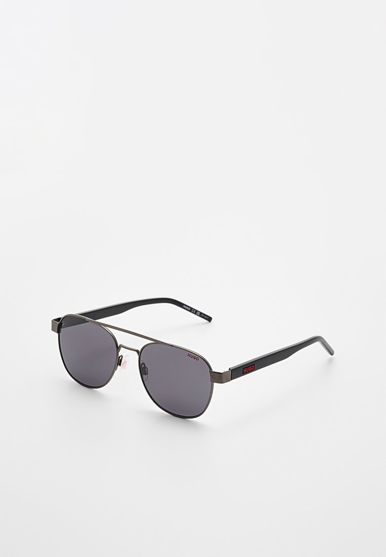 Schwarze Aviator-Sonnenbrille mit dunkel getönten Gläsern und dünnem Metallrahmen, versehen mit roten Hugo-Logos auf den Gläsern und Bügeln.