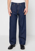 Locker sitzende dunkelblaue Jeans aus Denim, getragen mit schwarzen Lederschuhen und einem weißen Hemd, von der Mitte des Oberkörpers bis zu den Füßen zugeschnitten.