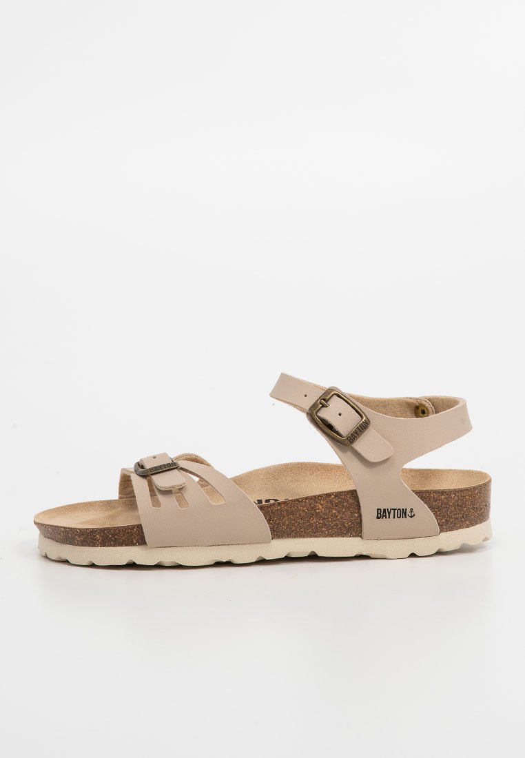 Hellbeige Sandale mit verstellbarem Riemen, Korkfußbett und weißer Gummisohle. Enthält dekorative Aussparungen und ein Detail mit einer Metall-Schnalle.