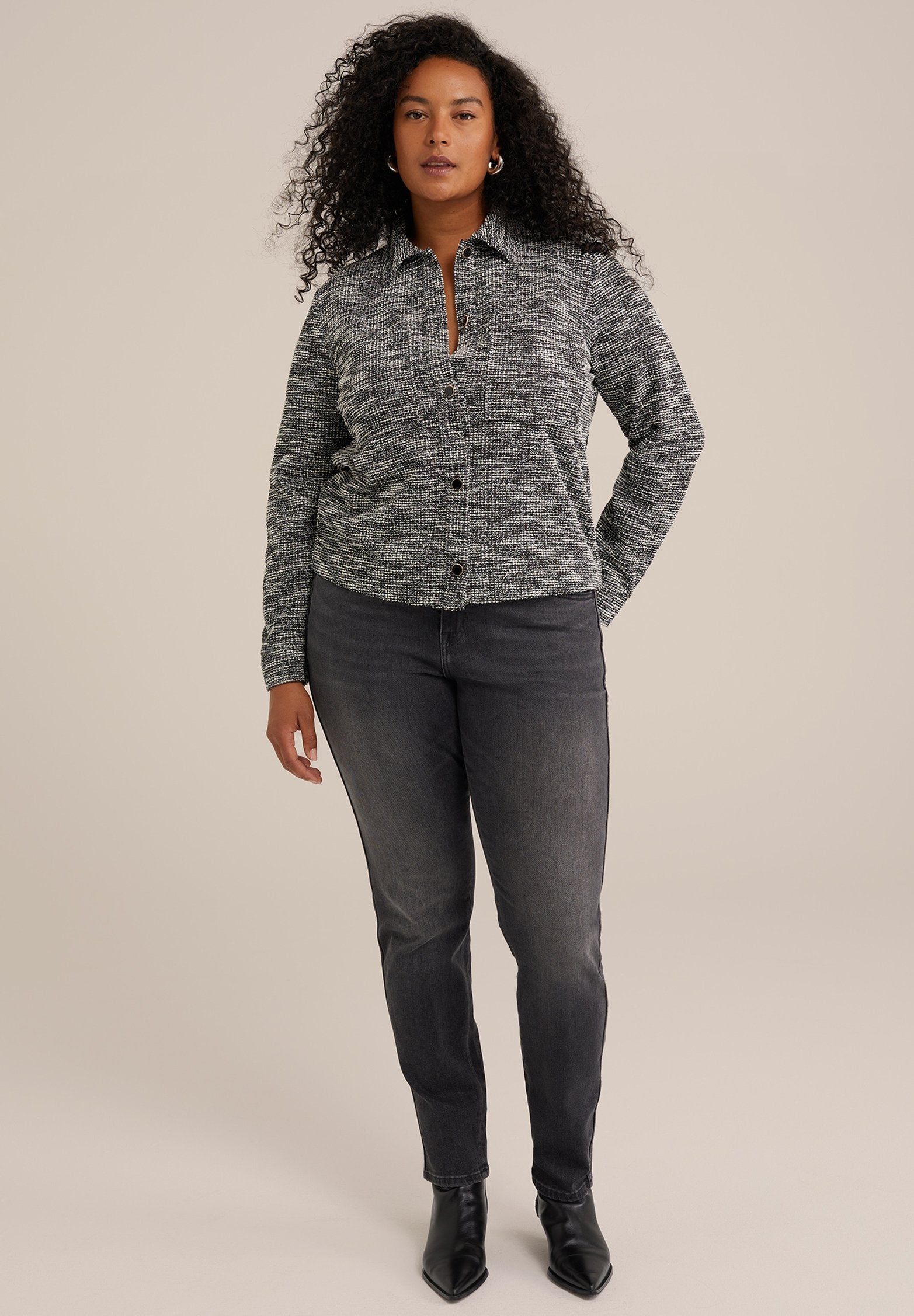 Grau und schwarz gemusterter Hemdchen-Pullover mit Kragen, kombiniert mit dunklen Jeans und schwarzen spitzen Stiefeln. Glatte Textur und taillierte Passform.