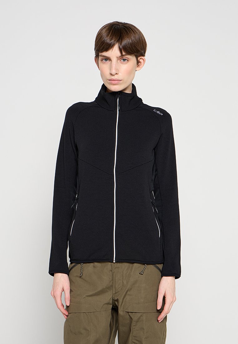 Schwarze Reißverschlussjacke aus strukturiertem Stoff mit hohem Kragen, weißem Reißverschluss und figurbetontem Schnitt, kombiniert mit Cargohosen.
