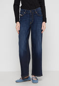 Dunkelblaue weit geschnittene Jeans mit klassischem Design, ausgestattet mit gelben Nähten und vorderen Taschen, kombiniert mit einem schwarzen Hemd und blauen Ballerinas.