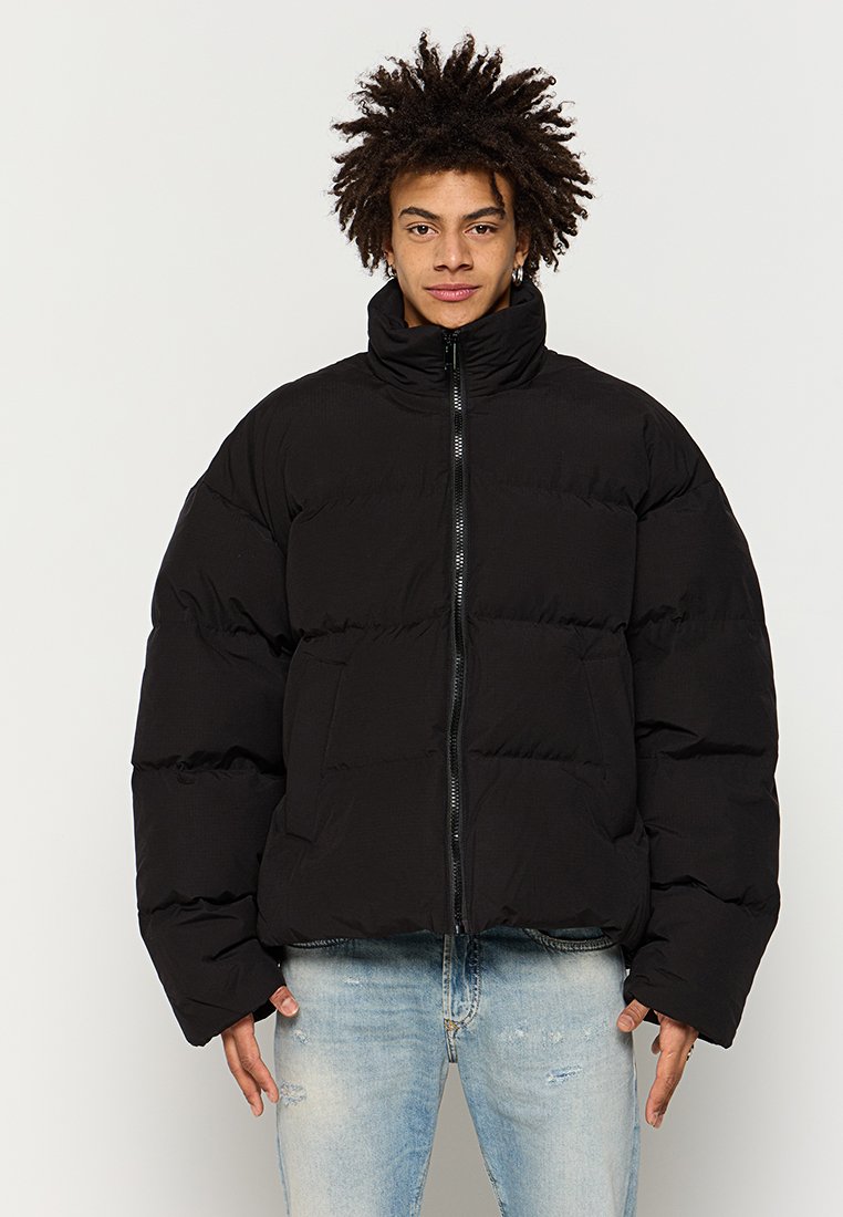 Schwarze Pufferjacke mit hohem Kragen, Frontreißverschluss und zwei seitlichen Taschen. Hat eine gesteppte Textur und eine lockere Passform.