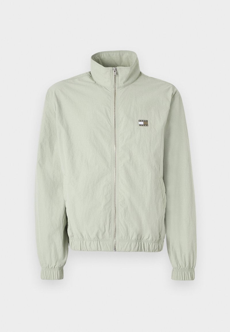 Hellgrüne Zip-Jacke mit hohem Kragen, gerafften Manschetten, elastischem Bund und einem kleinen Logo-Patch auf der linken Brust.