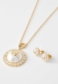 Goldkette mit einem großen kreisförmigen Anhänger, der eine perlenähnliche Mitte hat, umgeben von Kristallen. Passende goldene Ohrstecker mit ähnlichem Design.
