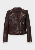 Bordeauxrote Leder-Bikerjacke mit silbernen Nieten, Reißverschlusstaschen und verschiedenen bestickten Patches mit Herzen und Sternen. Mit Gürteltasche in der Taille.