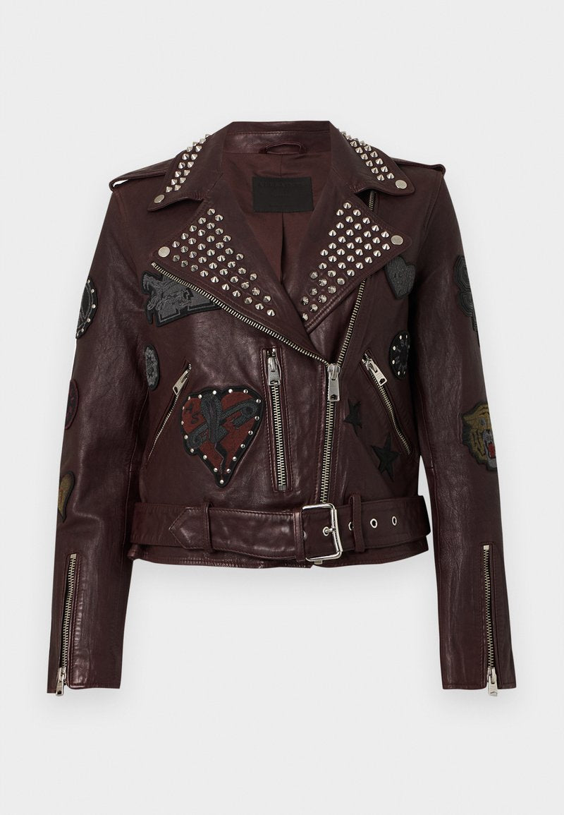 Bordeauxrote Leder-Bikerjacke mit silbernen Nieten, Reißverschlusstaschen und verschiedenen bestickten Patches mit Herzen und Sternen. Mit Gürteltasche in der Taille.