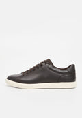 Braune Ledersneaker mit glatter Oberfläche, abgerundeter Spitze, sechs Ösen und kontrastierender, cremefarbener Gummisohle. Minimalistisches Design und nahtlose Verarbeitung.