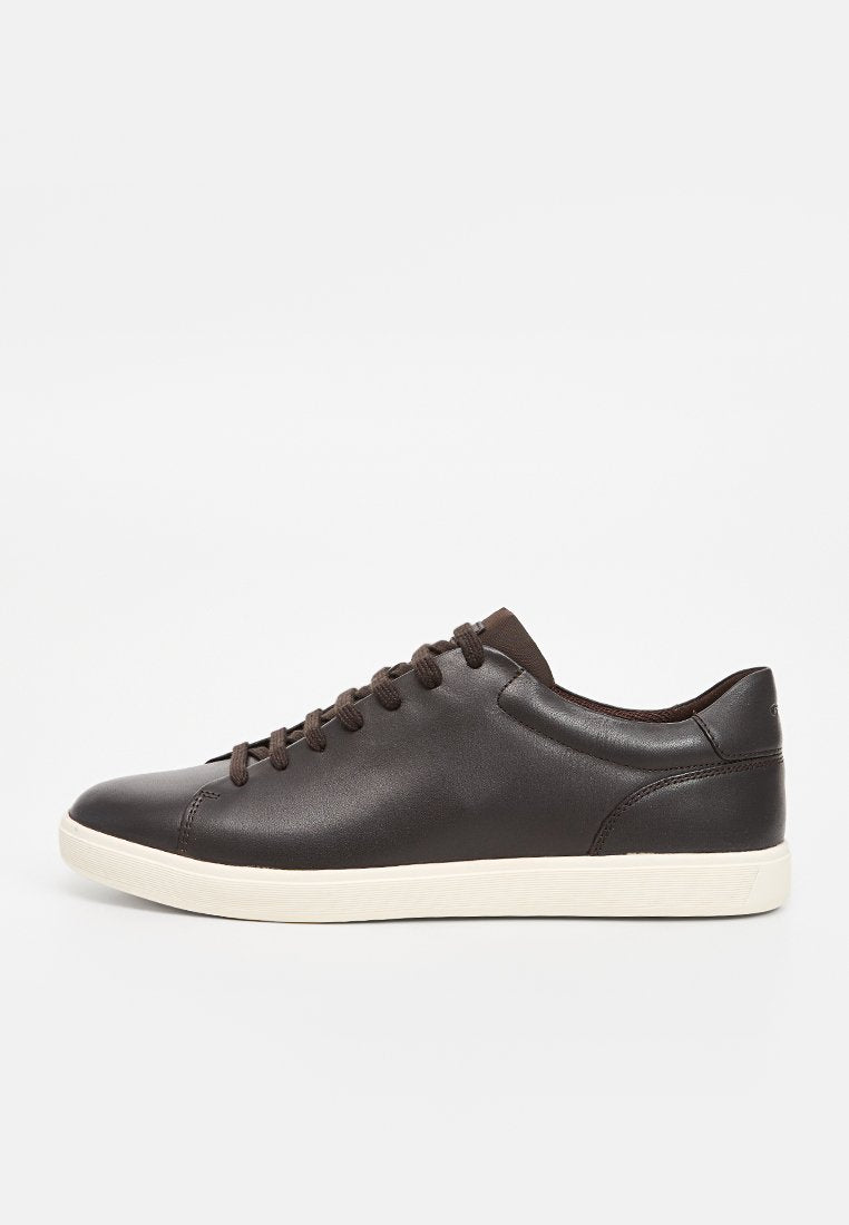 Braune Ledersneaker mit glatter Oberfläche, abgerundeter Spitze, sechs Ösen und kontrastierender, cremefarbener Gummisohle. Minimalistisches Design und nahtlose Verarbeitung.