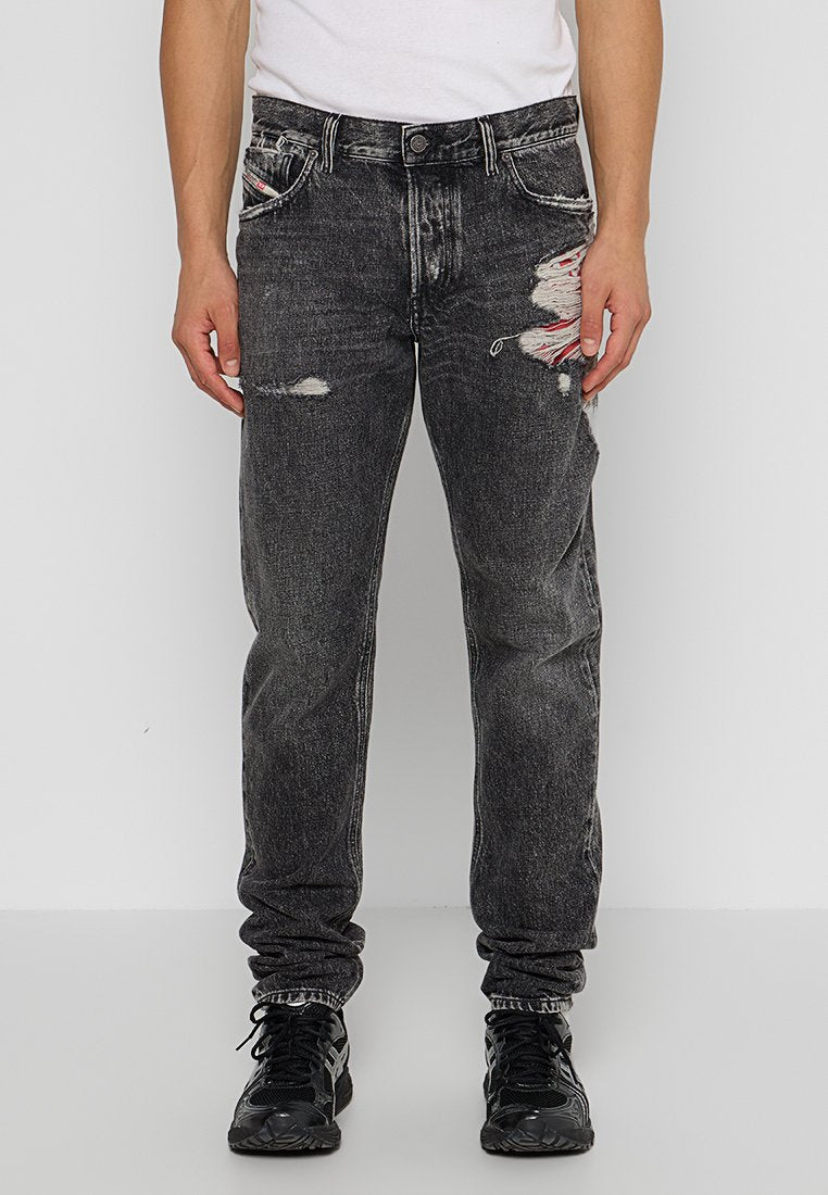 Schwarze, distressed Jeans mit lockerer Passform, versehen mit fransigen Details und einem verblassten Finish. Tragen mit schwarzen Sportschuhen.