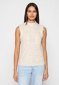 Ärmelloses Strickoberteil in Creme mit hohem Kragen, strukturierten Zopfmustern und figurbetontem Design. Kombiniert mit hellblauen Jeans.
