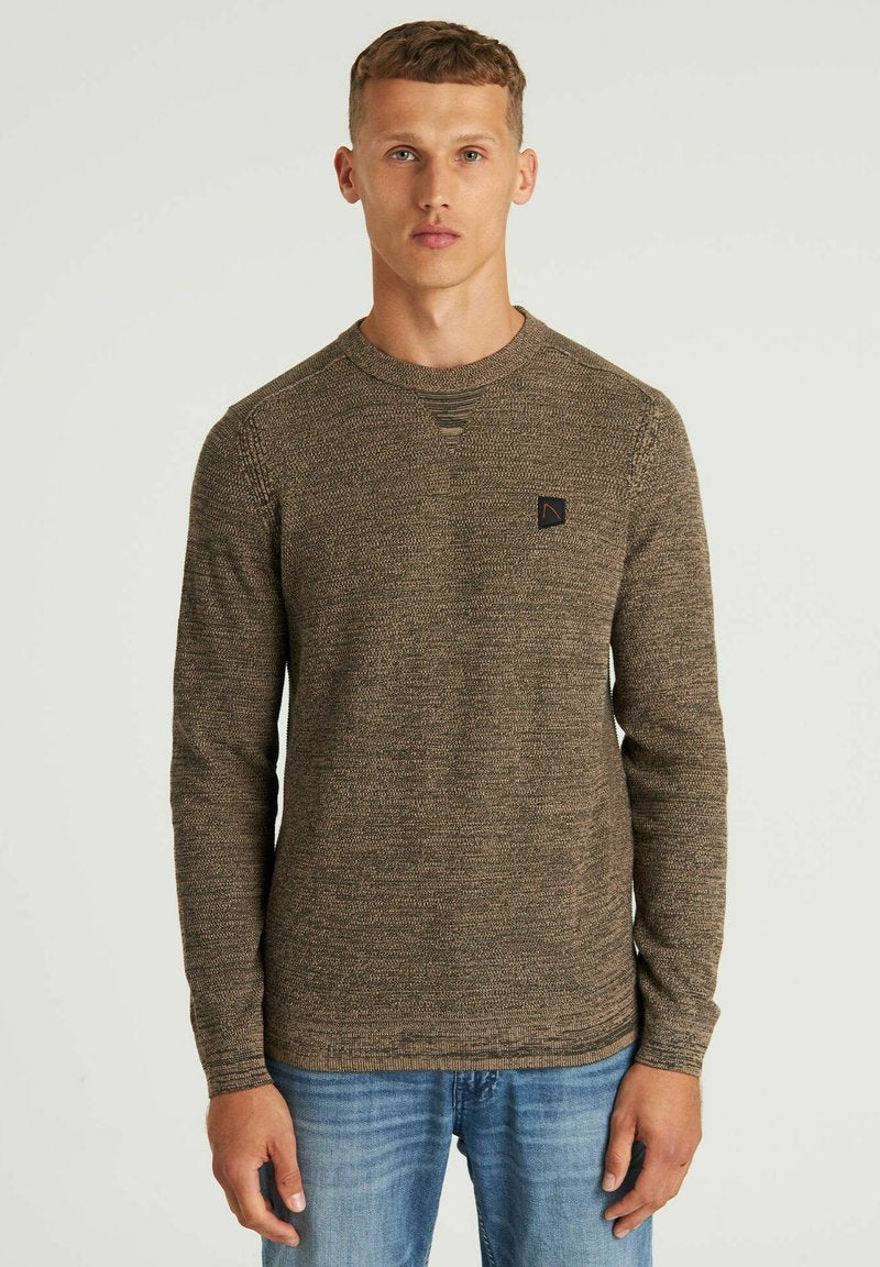 Braun strukturierter Pullover mit Rundhalsausschnitt, gerippten Bündchen und einem kleinen schwarzen Logo-Patch auf der Brust, kombiniert mit blauen Jeans.