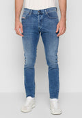 Mann in schlank geschnittenen blauen Jeans mit leichter Ausbleichung, weißen Socken und weißen Sneakers, vor einem schlichten hellgrauen Hintergrund stehend.