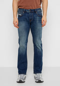 Person in geraden, ausgebleichten blauen Jeans und weiß-grauen Sportschuhen, der vor einem schlichten hellen Hintergrund steht.