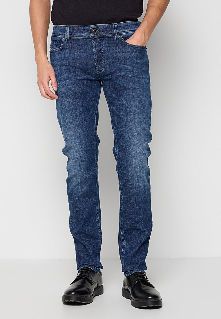 Blaue Denim-Jeans, gerade geschnitten, mit fünf Taschen, leichter Ausbleichung an den Oberschenkeln und einem dunklen Waschmittel. Kombiniert mit schwarzen Lederschuhen.
