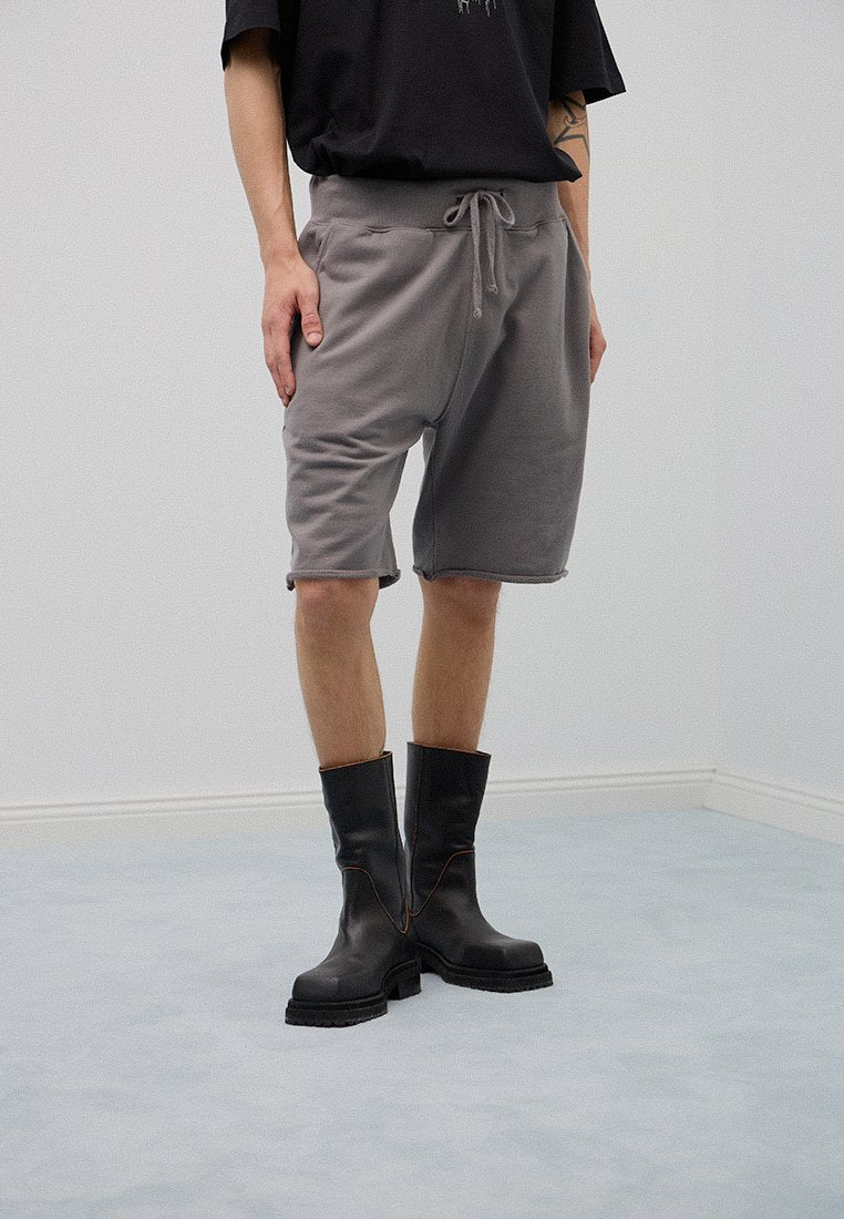 Graue Fleece-Shorts mit einem elastischen Bund und Kordelzügen, kombiniert mit schwarzen Stiefeln bis zur Mitte der Wade mit braunen Nähakzenten.