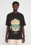 Ein junger Mann steht mit dem Gesicht zur Kamera und trägt ein schwarzes, übergroßes T-Shirt mit einer Basketball-Trophäe und dem Text "Pecador College Association".