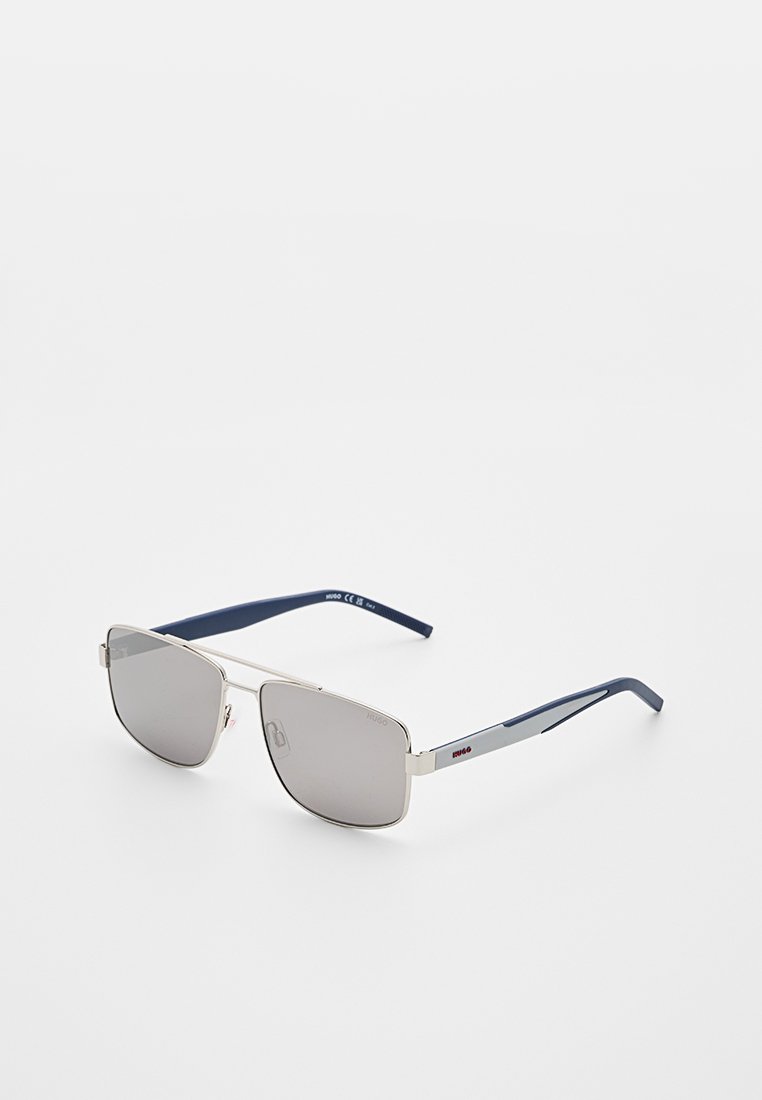 Sonnenbrille mit silbernem Metallrahmen, grauen Gläsern und dunkelblauen Bügeln, mit rotem Hugo-Logo an der Seite.