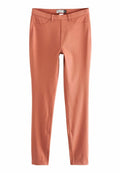 Schmal geschnittene, lange Leggings in gedämpftem Terrakotta mit Gürtelschlaufen, Fronttaschen und sichtbaren Nähten.