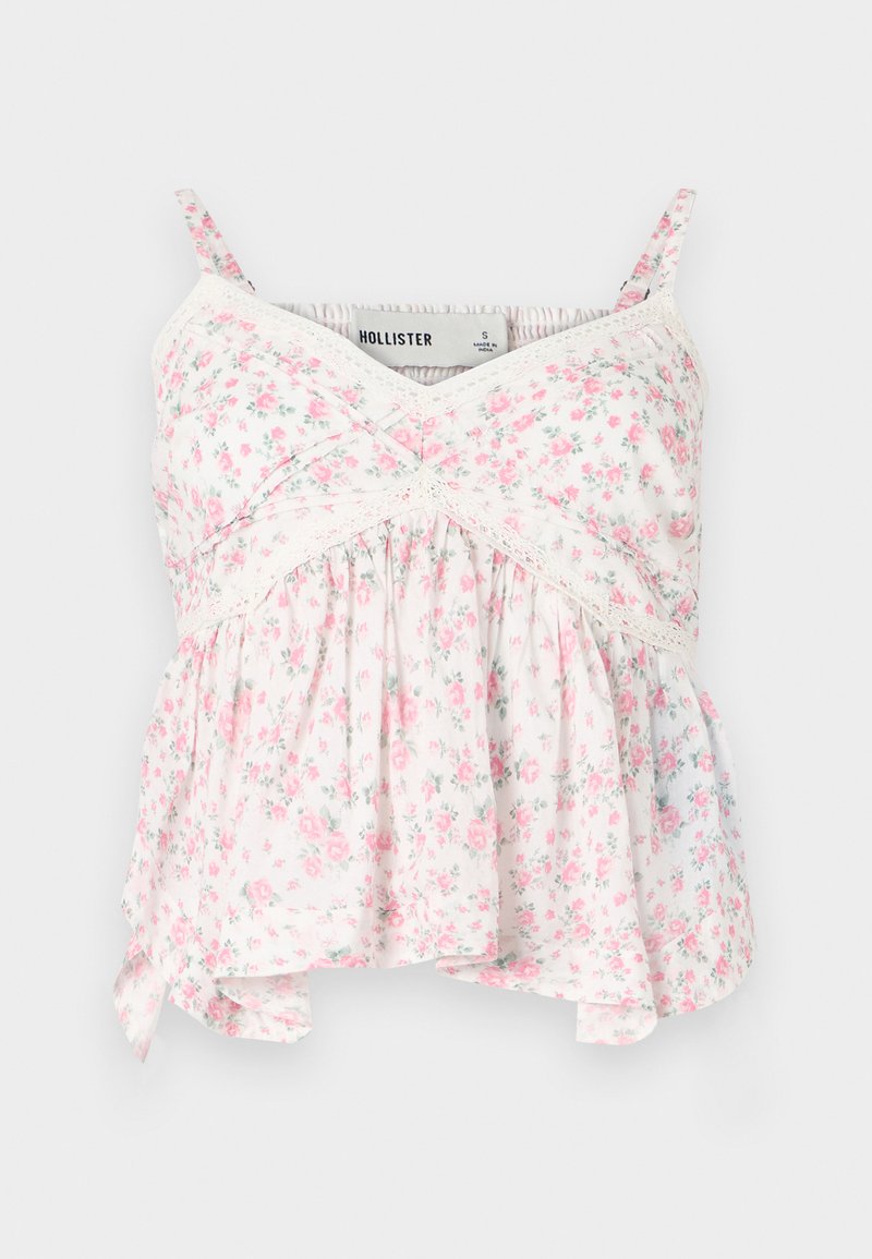 Floral Top mit weißem Hintergrund und pinken sowie grünen Blumen, Spitzendetails, figurbetontem Oberteil und einem lockeren, fließenden Saum.