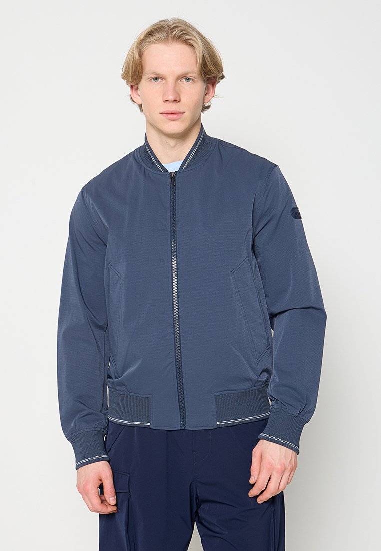 Marineblaue Bomberjacke mit Frontreißverschluss, gerippten Bündchen und Bund, Seitentaschen und minimalistischem Design. Glattes, leichtes Gewebe.