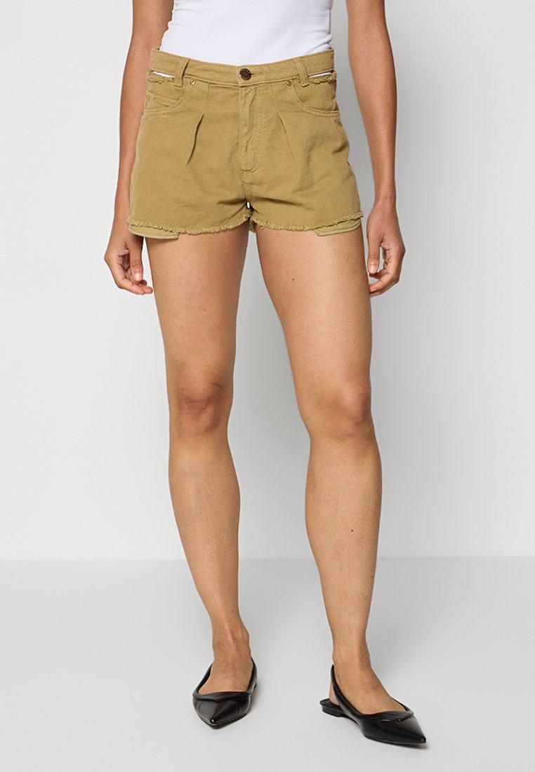 Khakifarbene Baumwollshorts mit ausgefranstem Saum, vorderen Abnähern und Reißverschluss. Kombiniert mit schwarzen spitz zulaufenden Ballerinas als Kontrast.