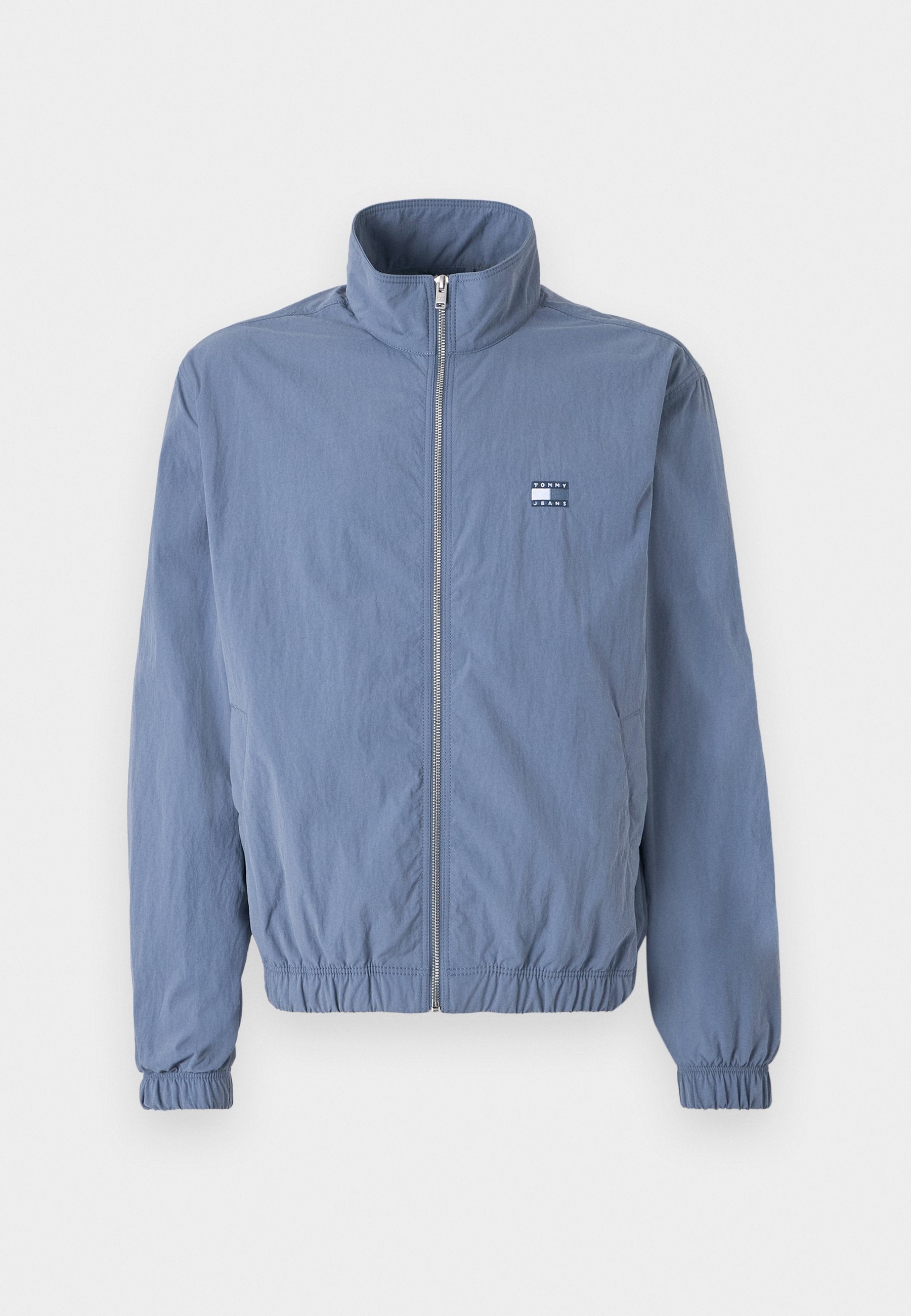 Hellblaue, mit Reißverschluss versehenen Jacke mit hohem Kragen, elastischen Bündchen und Taillenbund. Verfügt über ein kleines Logopatch auf der linken Brust.
