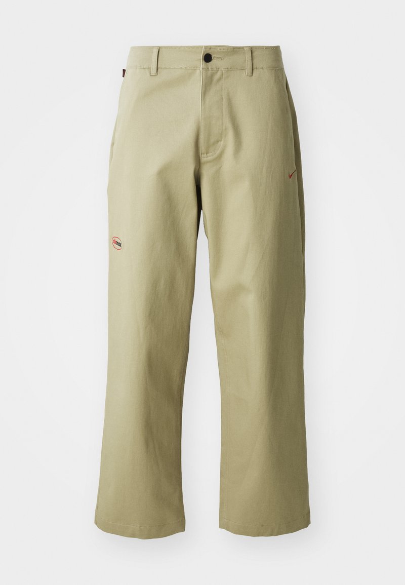 Beige weit geschnittene Baumwollhose mit Knopfverschluss, seitlichen Taschen und gesticktem roten Nike-Logo an der Seite.