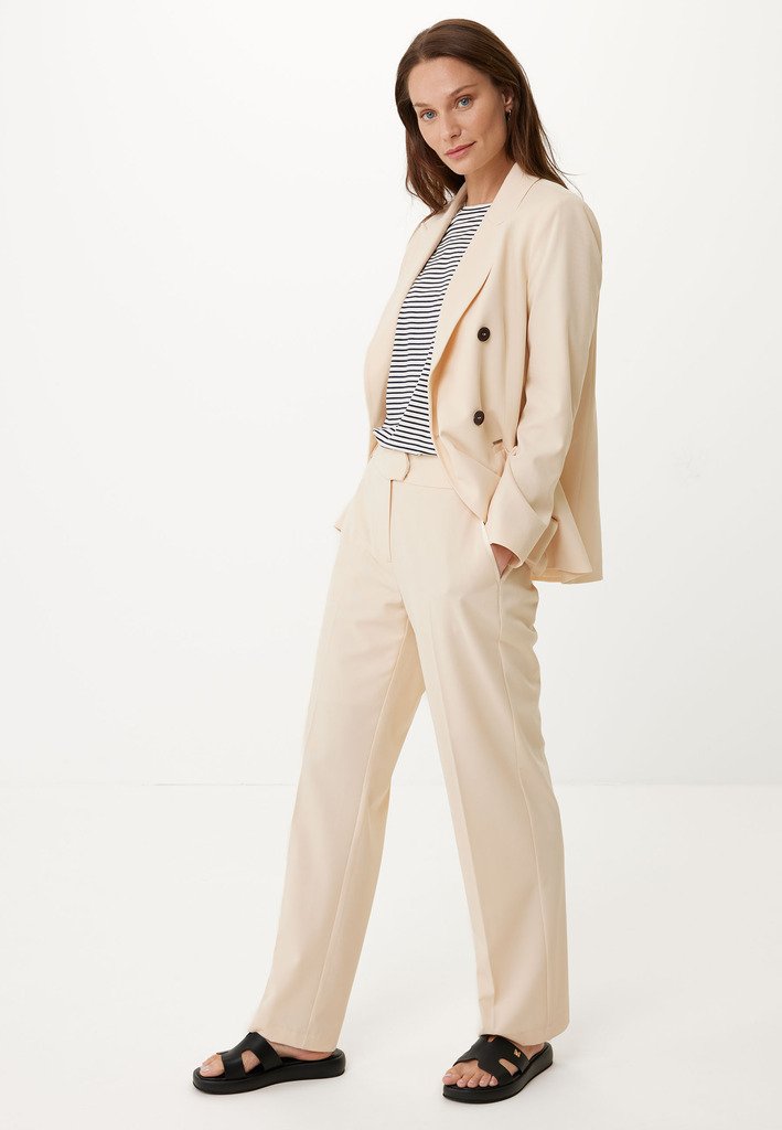 Beige maßgeschneiderter Anzug mit einem doppelt geknöpften Blazer und geraden Hosen, kombiniert mit einem gestreiften Hemd und schwarzen Sandalen.
