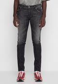 Mann trägt ausgewaschene schwarze Slim-Fit-Jeans und rote Sportschuhe, steht vor einem einfarbigen hellen Hintergrund.