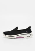 Schwarzer Slip-on-Sneaker mit weißer und lila Sohle, atmungsaktivem Mesh-Obermaterial und markierter Fußgewölbestütze, die an der Ferse sichtbar ist.