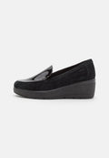 Schwarze Slipper aus Wildleder mit glänzenden Lacklederakzenten. Merkmale sind ein Keilabsatz und ein abgerundetes Design. Leicht und flexibel.