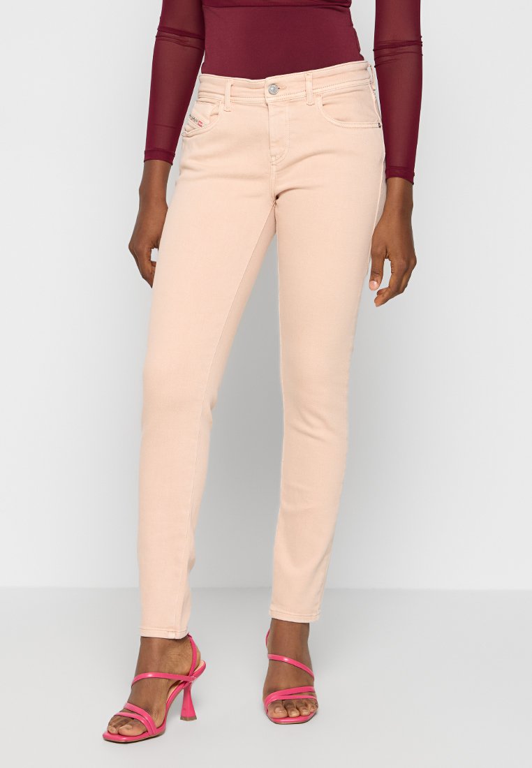 Helle rosa Skinny-Jeans mit glatter Textur, fünf Taschen und Metallknopfverschluss. Kombiniert mit leuchtend rosa hohen Sandalen mit Riemen.