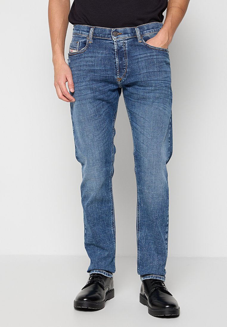 Blaue Denim-Jeans mit geradem Bein, kontrastierenden Nähten, Fünf-Taschen-Design und einer leicht ausgewaschenen Textur. Schwarze Schuhe getragen.