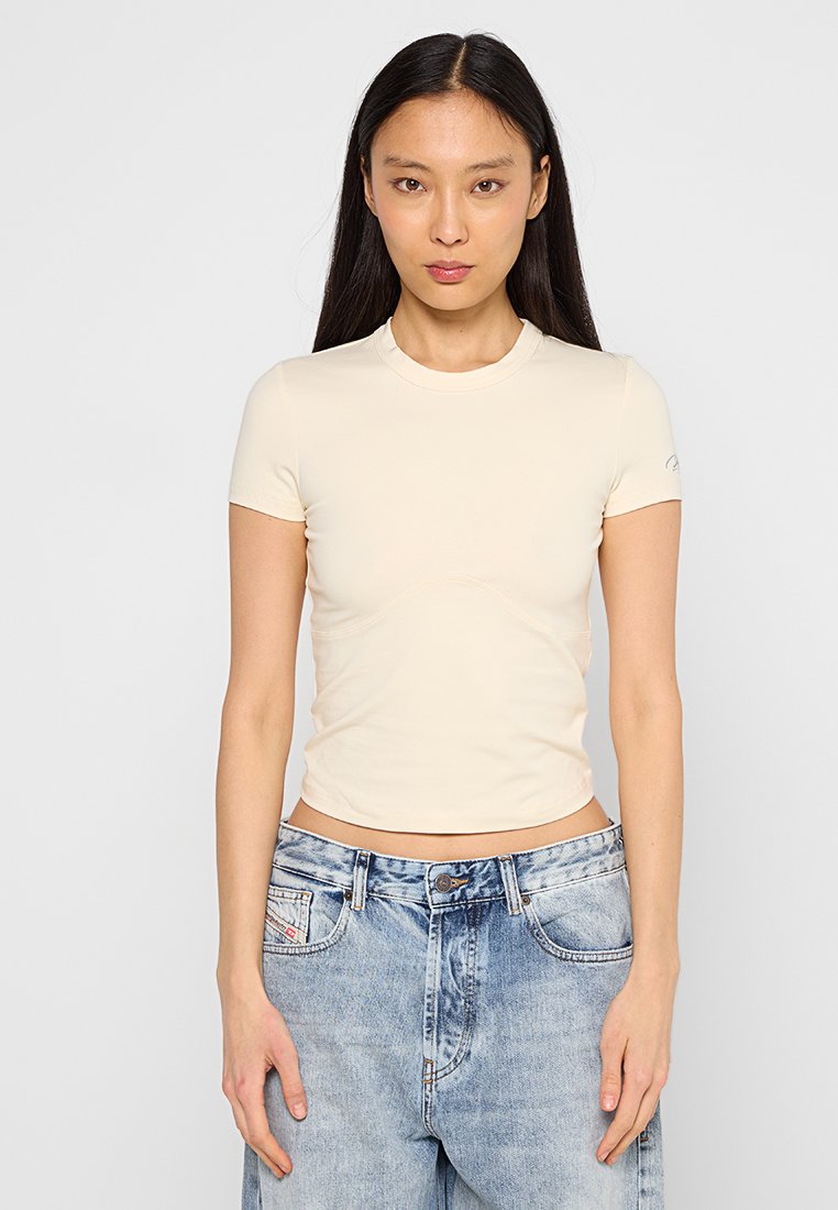 Beige, tailliertes T-Shirt mit kurzen Ärmeln aus glattem Stoff, mit rundem Halsausschnitt und subtilen Nähten. Getragen mit hellblauen Denim-Jeans.