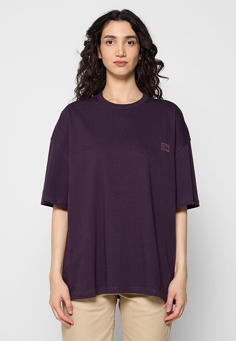 Lila übergroßes T-Shirt mit geripptem Stoff, Rundhalsausschnitt und kurzen Ärmeln. Verfügt über ein kleines Logo-Patch auf der Brust.