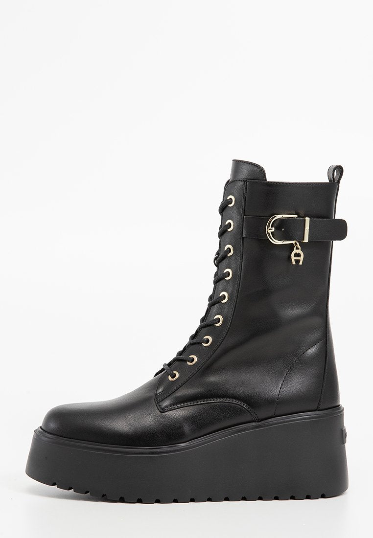 Schwarze Kunstleder-Ankle Boots mit Plattformsohle, dicken Schnürsenkeln, goldenen Ösen und einem seitlichen Schnallendetail. Glatte Textur und runde Zehenform.