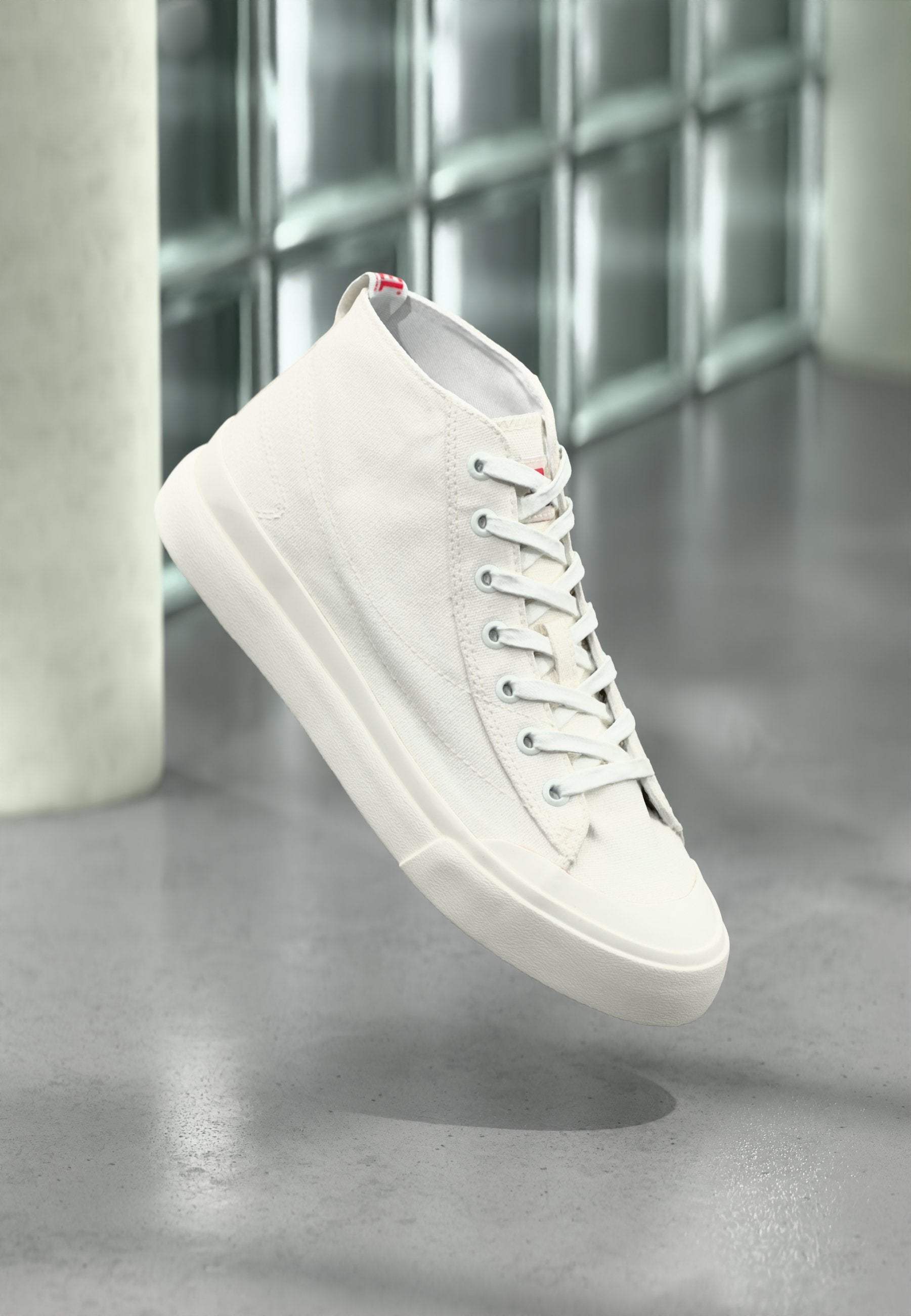Weiße Canvas-High-Top-Sneaker mit strukturierter Oberfläche, flachen Schnürsenkeln und einer Gummisohle. Versehen mit einem kleinen roten Logo auf der Zunge.