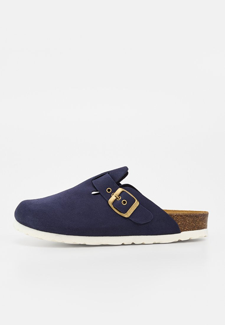 Marineblauer Slipper mit Messingschnallenriemen, Korkfußbett und weißer, strukturierter Sohle, seitlich auf weißem Hintergrund dargestellt.
