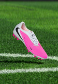 Weißer und rosa Nike Fußballschuh mit schwarzem Swoosh schwebt über grünem Gras nahe einer weißen Spielfeldlinie.