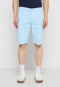 Männliche Person trägt hellblaue knielange Shorts, weiße Socken und weiße Turnschuhe, steht vor einem einfarbigen hellgrauen Hintergrund.