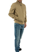 Beige leichte Jacke mit Stehkragen, Reißverschluss und Seitentaschen, kombiniert mit blauen Jeans. Der Stoff wirkt glatt und leicht glänzend.