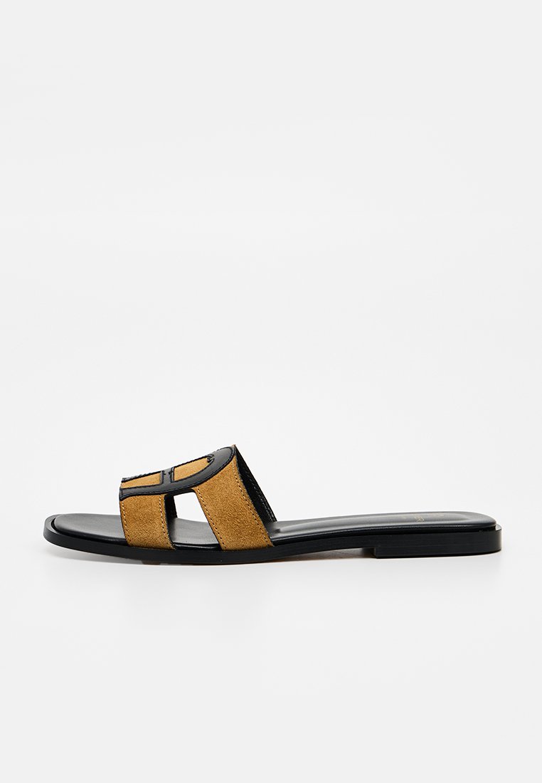 Flache Sandale mit schwarzer Sohle und senffarbenen Wildlederriemen mit ausgeschnittenem geometrischem Design.