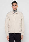 Helle beige Bomberjacke mit Reißverschluss, flachem Kragen, seitlichen Taschen und elastischen Bündchen, aus glattem Stoff, auf einem Modell präsentiert.