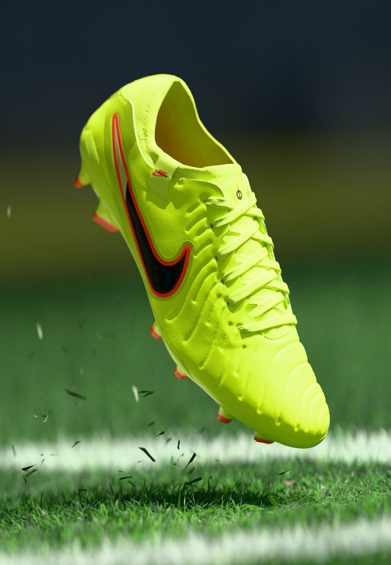 Nike-Fußballschuh, leuchtend gelb mit schwarzem Swoosh, strukturierte Oberseite, erhabenes Muster und orangefarbene Akzente, schwebt über einem Grasfeld.