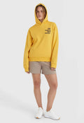 Gelbe Kapuzenjacke mit schwarzem Schriftzug, lockere Passform, Kapuze mit Kordelzug, kombiniert mit beigen Shorts und weißen Turnschuhen. Glatter Stoff, lässiger Stil.